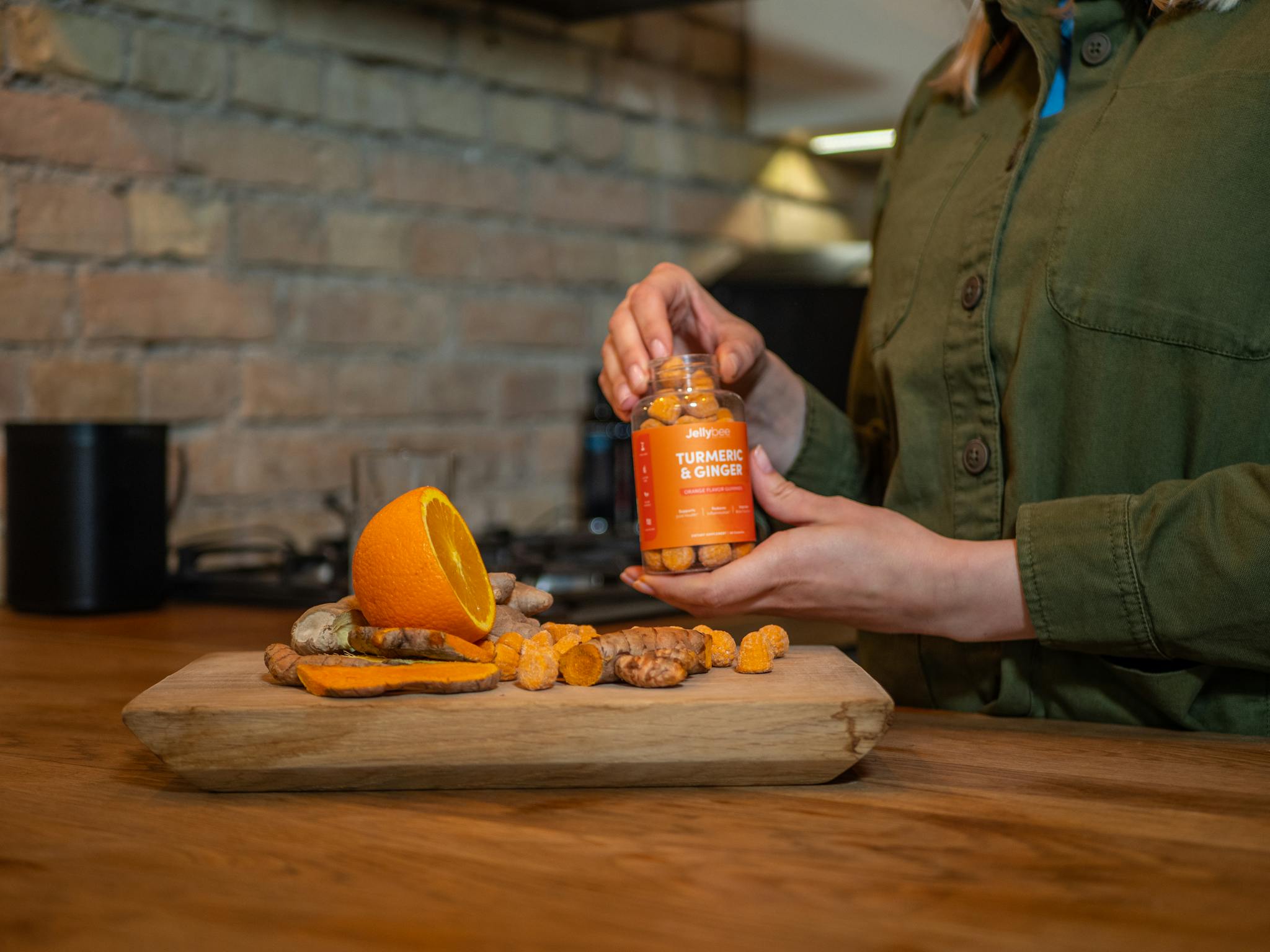 A person holding a turmeric and ginger supplement bottle next to sliced fresh ingredients in a kitchen setting.
