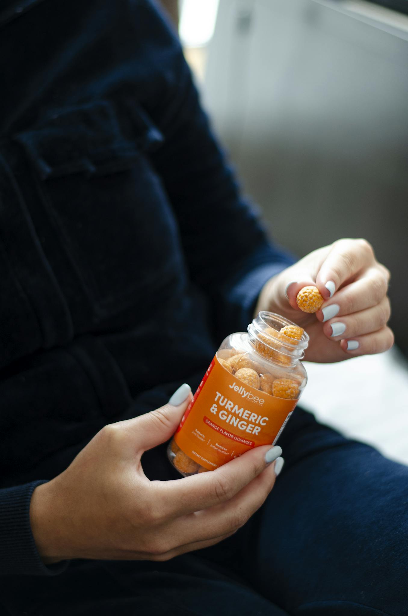 Close-up of a person holding turmeric and ginger gummies in a bottle with natural lighting.