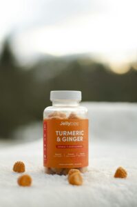 Close-up of Jellybee turmeric and ginger gummies bottle outdoors on snow, with gummies scattered around.