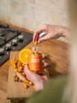 Hands holding Jellybee turmeric and ginger gummies bottle over a wooden board with ingredients.
