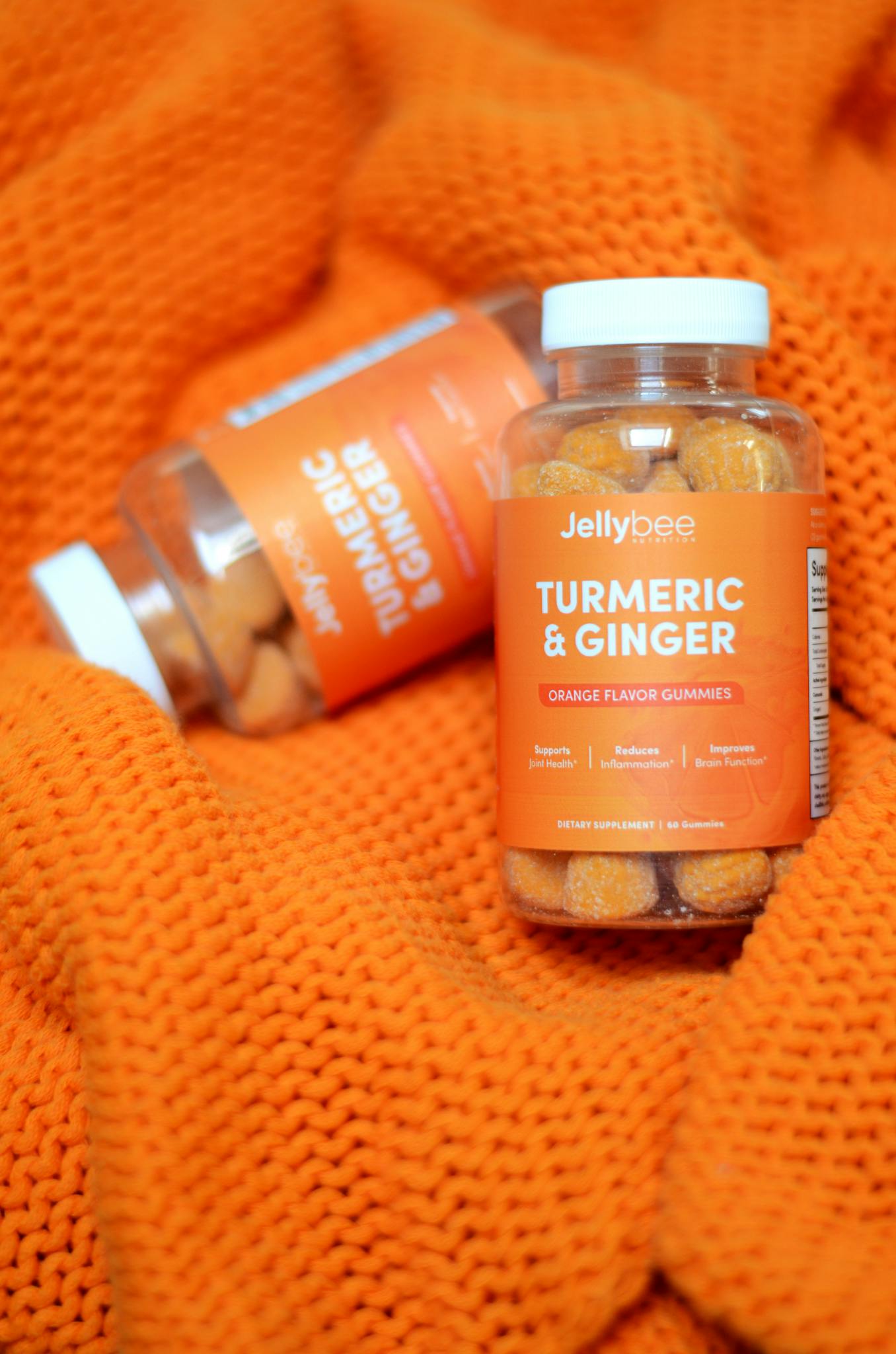 Vibrant turmeric and ginger gummies bottle displayed on textured orange fabric.